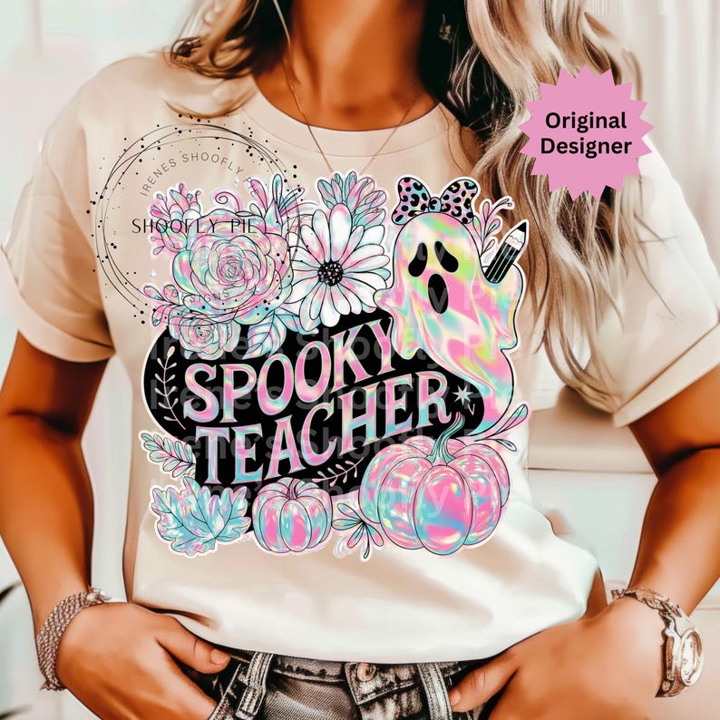 May include: Beige t-shirt featuring a colorful graphic with the words "Spooky Teacher." The design includes a ghost, pumpkins, flowers, and a pencil. The shirt has short sleeves and a round neckline.