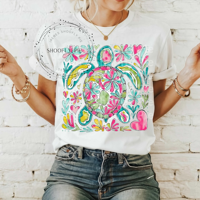 May include: White t-shirt with a colorful graphic of a sea turtle surrounded by flowers and hearts. The turtle is outlined in teal and filled with a variety of colors, including pink, yellow, green, and blue.