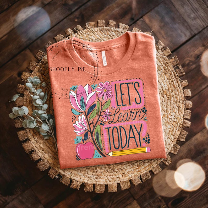 May include: A peach coloured t-shirt with a floral design and the text "Let's Learn Today" in a colourful font. A yellow pencil and a red apple are also included in the design.
