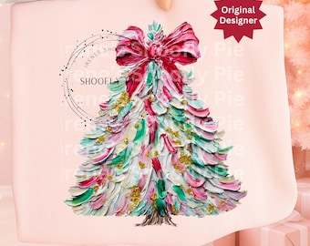 May include: A pink tote bag with a Christmas tree design. The tree is painted with green, pink, and white brushstrokes, gold flecks, and a red bow. The bag has the text "SHOOFly Pie" and "Original Designer" on it.