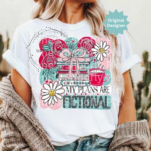 May include: White t-shirt featuring a colorful graphic with books, flowers, and a coffee cup. The text "MY PLANS ARE FICTIONAL" is displayed in a playful font. The design includes pink, teal, and black accents.