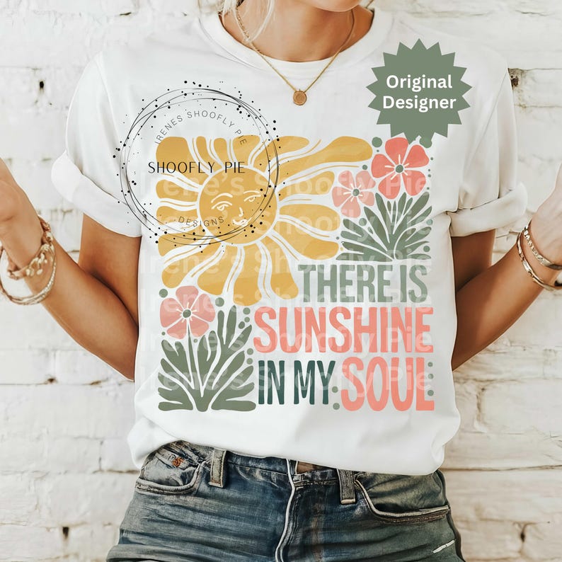 May include: White t-shirt with a colorful graphic design. The design features a yellow sun, pink and orange flowers, and the text "THERE IS SUNSHINE IN MY SOUL" in various colors. The shirt has short sleeves.