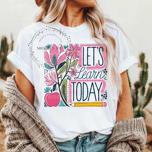 May include: White t-shirt with a colourful graphic design featuring flowers, an apple, and a pencil. The text "Let's Learn Today" is written in a playful font.