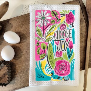 May include: White kitchen towel with a colorful floral design and the text "Choose Joy". The design features pink, green, yellow, and blue colors.