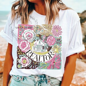 May include: White t-shirt with a floral design featuring a house and the word "REALTOR".
