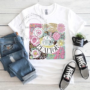 May include: White t-shirt featuring a floral design with the word "REALTOR" in the centre. The design includes a small house and various flowers in pink, yellow, and green.