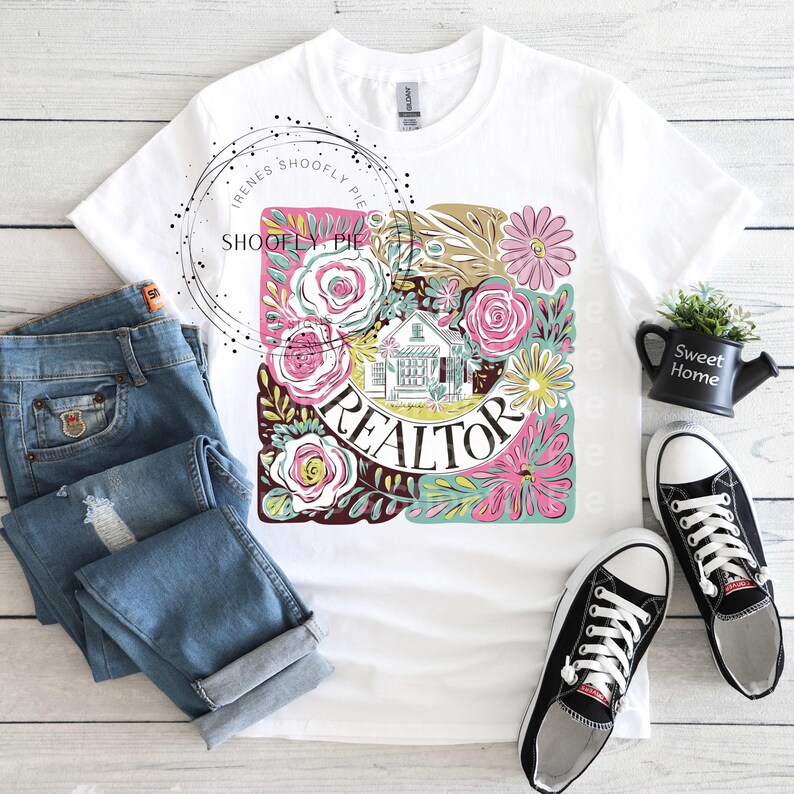 May include: White t-shirt featuring a floral design with the word "REALTOR" in the centre. The design includes a small house and various flowers in pink, yellow, and green.