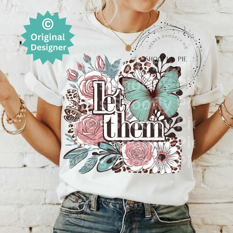 May include: White t-shirt with a floral and butterfly design. The text "Let them" is printed on the shirt.
