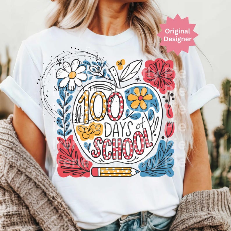 May include: White t-shirt with a colourful graphic celebrating "100 Days of School." The design features an apple shape filled with text and floral elements in red, yellow, and blue, along with a pencil illustration.