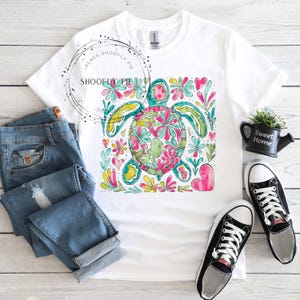 May include: White t-shirt with a colorful graphic of a sea turtle surrounded by flowers and hearts. The turtle is green, blue, yellow, and pink.