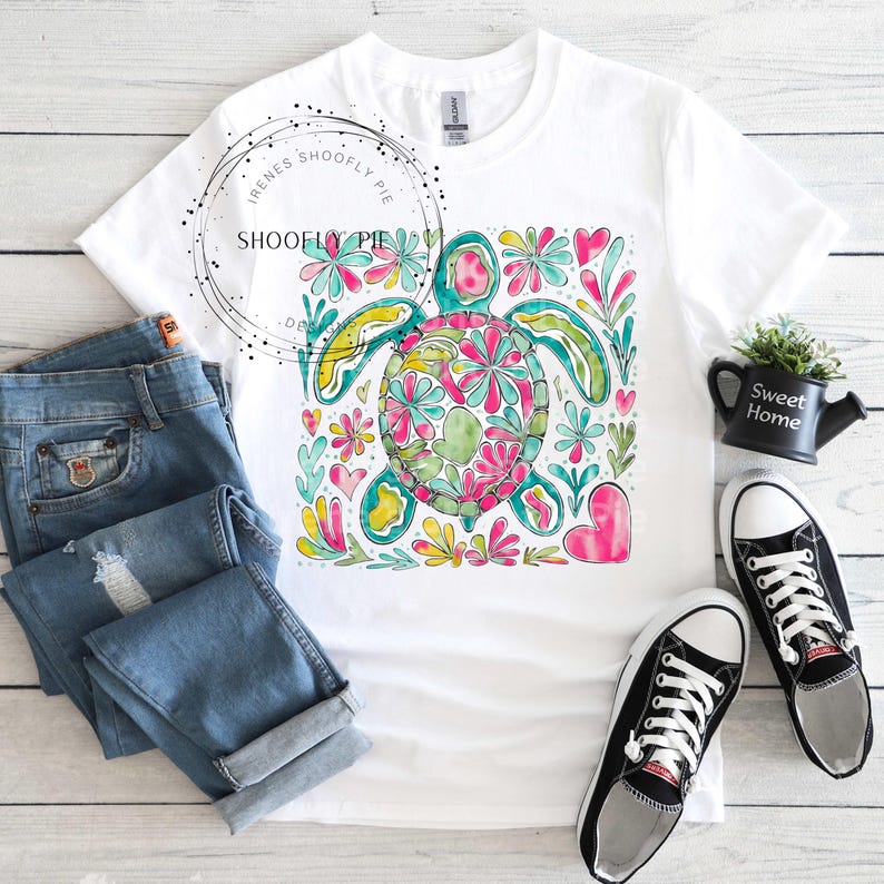 May include: White t-shirt with a colorful graphic of a sea turtle surrounded by flowers and hearts. The turtle is green, blue, yellow, and pink.