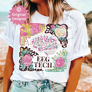 以下が含まれることがあります： 白いTシャツに、花柄のデザインと「EEG TECH」の文字がプリントされています。デザインには、心臓の鼓動の線が入った脳と、ピンクと黄色の花が含まれています。