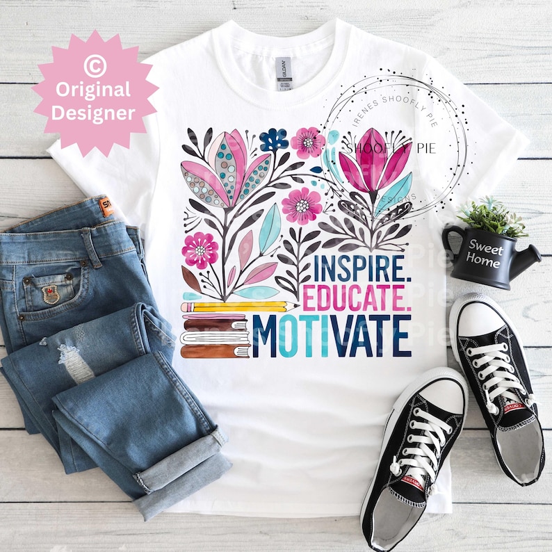 Op de afbeelding: Wit T-shirt met een bloemenontwerp in roze, blauw en zwart, en de woorden "INSPIRE. EDUCATE. MOTIVATE." De afbeelding bevat een blauwe spijkerbroek en zwart-witte sneakers. Een kleine zwarte gieter met "Sweet Home" is ook zichtbaar.