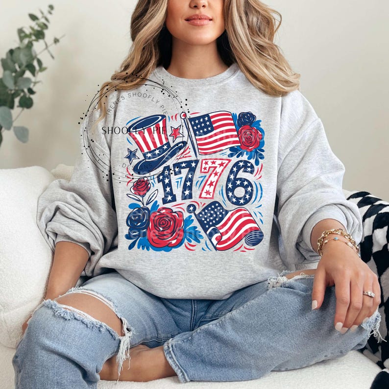May include: A gray sweatshirt with a graphic design featuring red, white, and blue stars, stripes, and a top hat. The graphic also includes the text "1776" and red roses.
