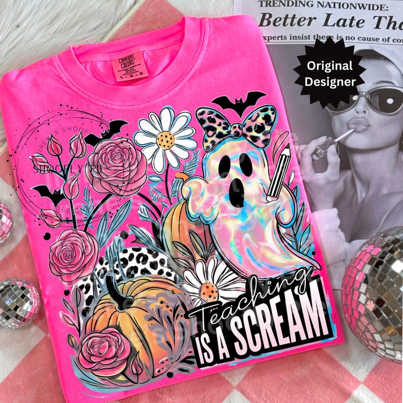 May include: A bright pink Comfort Colors t-shirt featuring a colorful graphic. The design includes a ghost holding a pencil, pumpkins, flowers, and the text "Teaching is a Scream". A bat-shaped bow and other Halloween-themed elements complete the design.