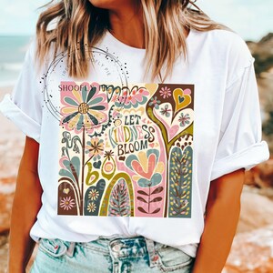 May include: White t-shirt with a colorful graphic design featuring flowers, hearts, and the text "Let Kindness Bloom".