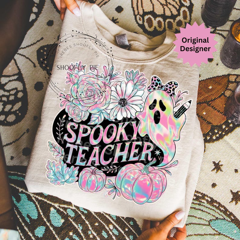 May include: A beige sweatshirt with a colorful graphic that says "Spooky Teacher." The design includes a ghost with a pencil, flowers, and pumpkins. The design has a pastel rainbow color scheme.