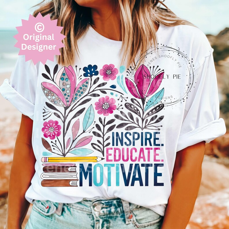 Op de afbeelding: Wit T-shirt met een bloemenontwerp in roze, blauw en paars, met de woorden "Inspire. Educate. Motivate." Het ontwerp bevat ook een potlood en boeken.