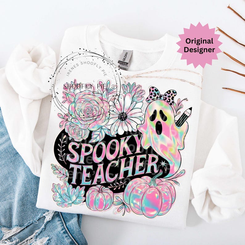 May include: White sweatshirt with a colorful graphic featuring a ghost holding a pencil, flowers, and pumpkins. The text "Spooky Teacher" is displayed in a black oval. The design includes pastel pink, blue, and yellow hues.