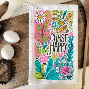 May include: White kitchen towel with a colorful floral design and the text "CHASE HAPPY" in black.