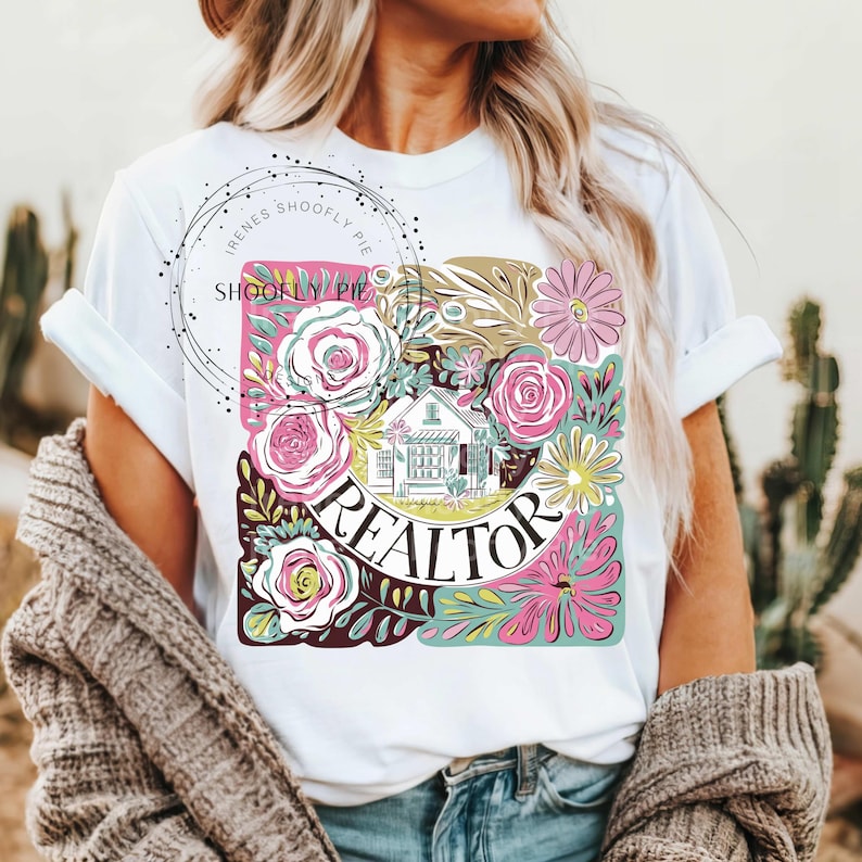 May include: White t-shirt featuring a floral design with the word "REALTOR" in a circle. The design also includes a small house and the text "Irene's Shoofly Pie".
