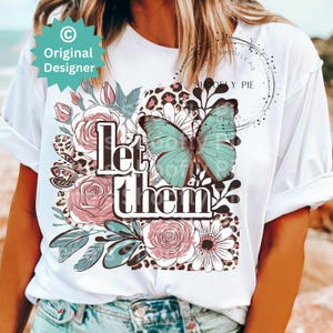 May include: White t-shirt with a floral design, a butterfly, and the text "Let them" printed on the front.