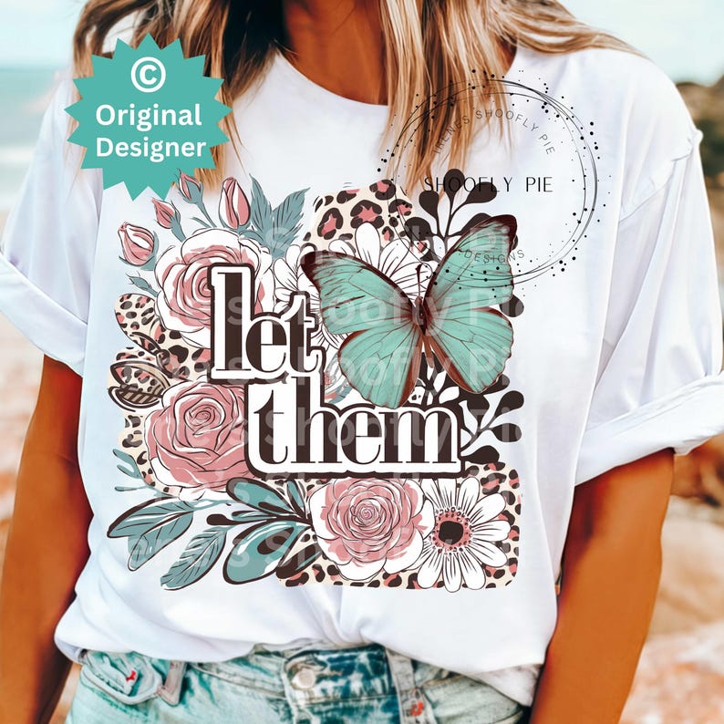 May include: White t-shirt with a floral design, a butterfly, and the text "Let them" printed on the front.