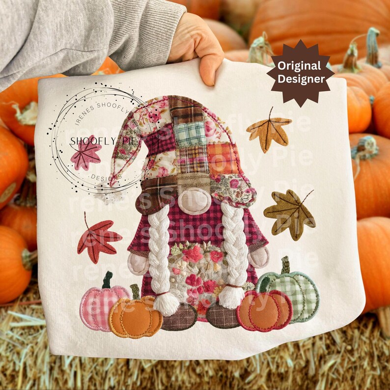 Peut inclure: Un coussin d&eacute;coratif cr&egrave;me avec un motif de gnome d'automne. Le gnome a un chapeau et une robe en patchwork, avec de longues tresses blanches. Des citrouilles et des feuilles d'automne entourent le gnome. Le texte "SHOOFY PIE DESIGN" est imprim&eacute; sur le coussin.