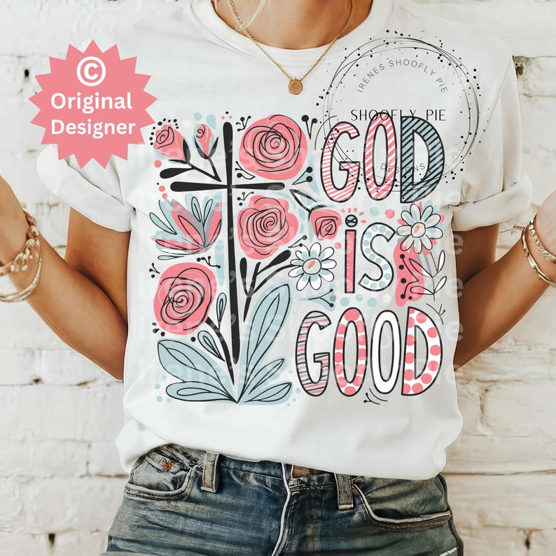 以下が含まれることがあります： 白いTシャツに花柄のデザインと「God is good」というピンクと黒の文字が書かれています