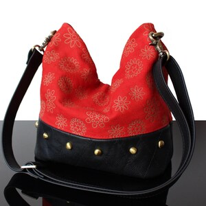 Peut inclure: Un sac à main de style hobo avec une section supérieure rouge vif ornée d'un motif floral doré répétitif et une section inférieure noire à texture matelassée. Le sac comprend des clous métalliques dorés le long de la couture et une bandoulière noire.