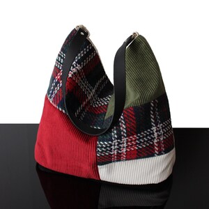 Peut inclure: Un sac hobo composé d'un patchwork de tissus, incluant du velours côtelé rouge, vert olive et blanc, ainsi qu'un textile à carreaux rouges, verts et blancs. Le sac est doté de deux anses noires fixées sur le dessus par des éléments métalliques.