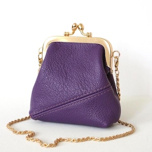 May include: A small, purple leather coin purse with a gold-colored clasp and chain strap. The purse has a textured surface and a kiss-lock closure. The chain is a delicate, twisted design.