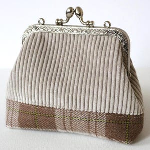 Peut inclure: Un porte-monnaie en velours côtelé beige avec un fermoir argenté. Le bas du sac présente un motif à carreaux marron et vert. Le sac est de forme rectangulaire.
