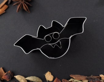 Könnte beinhalten: Ein Ausstecher aus Metall in Form einer Fledermaus mit zwei Augen und Zähnen. Der Ausstecher ist schwarz und hat eine glänzende Oberfläche.