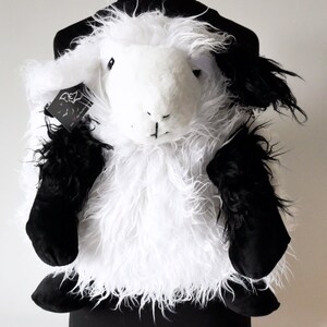 Può includere: Un giocattolo di peluche di pecora bianco e nero con una texture soffice. La pecora ha la pelliccia nera sulle gambe e sulla testa.