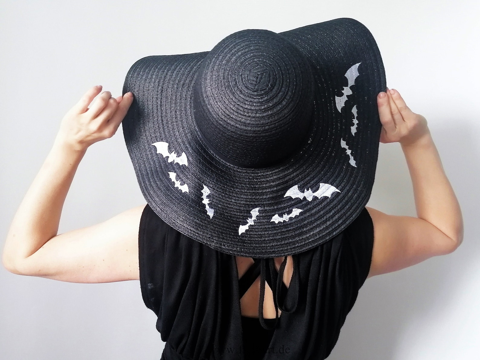 Black sun hat with white embroidered bats, worn by person in black dress—perfect whimsical touch for a summer goth beach day.