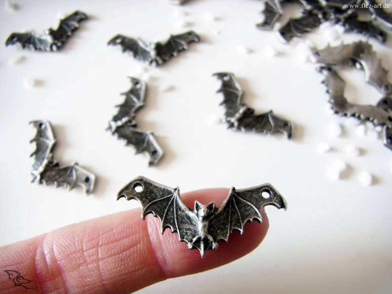May include: Silver-toned metal bat charms with detailed wings and a hanging bat design. The charms have two holes for attaching to jewelry or crafts.