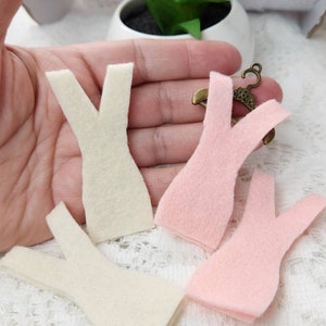 May include: Four felt fabric doll dress patterns, two white and two pink, with a small metal hanger.