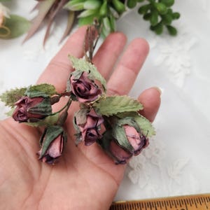 Pu&ograve; includere: Primo piano di un gruppo di piccole rose artificiali in varie tonalit&agrave; di rosa e viola, con foglie verdi. Le rose sono raggruppate e sembrano essere fatte di carta o tessuto. L'estetica generale &egrave; delicata e vintage.