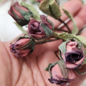Pu&ograve; includere: Primo piano di diversi piccoli boccioli di rosa artificiali nei toni del rosa e del viola. I boccioli di rosa hanno foglie e steli verdi. L'immagine &egrave; un primo piano, che mostra i dettagli dei fiori.