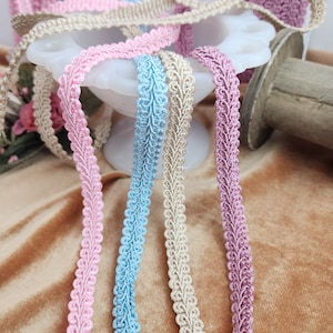 May include: Four spools of decorative trim with scalloped edges. The trim is in pink, light blue, beige, and mauve.
