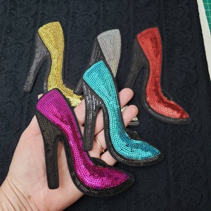 May include: Five sequined high heel shoe patches in different colors: gold, silver, turquoise, red, and pink. The patches are on a black lace fabric background.
