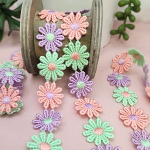 May include: A spool of pastel green, pink, and purple floral lace trim. The trim features a repeating pattern of small, embroidered flowers.