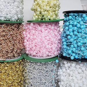 May include: Spools of beaded garland in various colors, including white, gold, silver, pink, and turquoise. The beads are strung together, creating a decorative chain. Ideal for crafts, decorations, and embellishments.