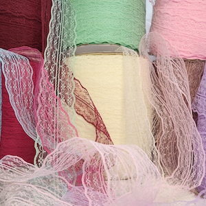 May include: Assortment of lace trim spools in various colors, including light blue, burgundy, pink, green, and lavender. The lace trim is delicate and has a wavy pattern.
