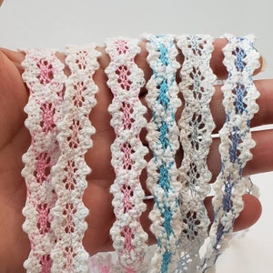 May include: Five different lace trims in various colors, including pink, blue, and white. The trims are delicate and have a scalloped edge.