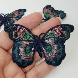 May include: Two embroidered butterfly patches in dark blue, green, and pink. The butterflies have a detailed design with a layered look.