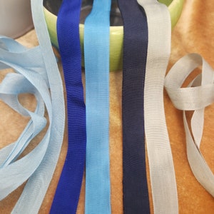 May include: Six different colors of ribbon, including blue, light blue, navy blue, and gray. The ribbons are arranged in a row on a green surface.