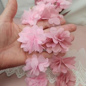 May include: Pink flower trim with a delicate mesh backing. The trim is made of soft, layered fabric and is perfect for adding a touch of femininity to any project.