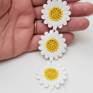 May include: White daisy flower trim with yellow centers. The trim is made of crocheted fabric and is perfect for adding a touch of whimsy to any project.